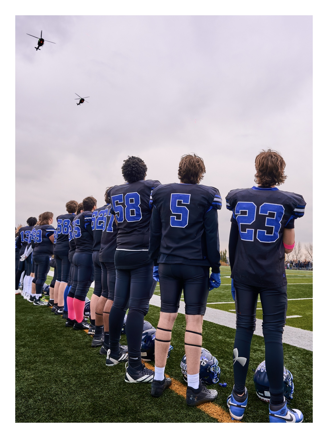 Football team standing together on the sideline as helicopters fly overhead