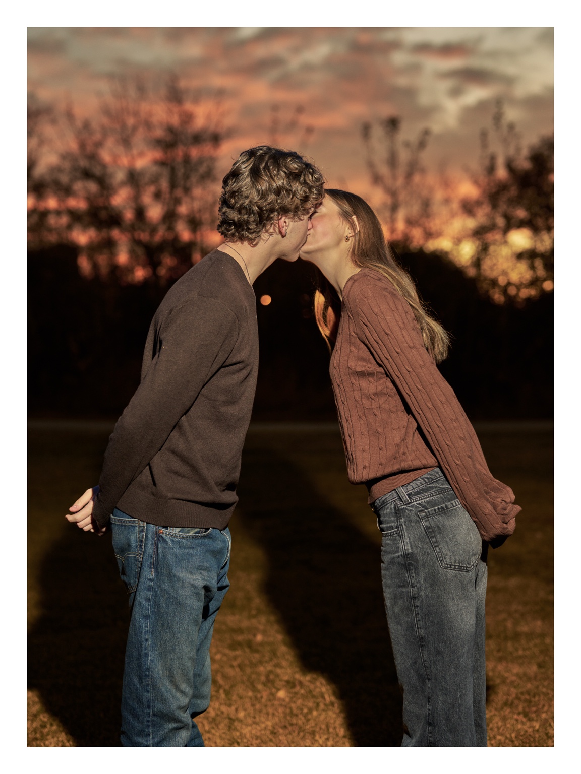 A couple kissing beneath a warm sunset sky