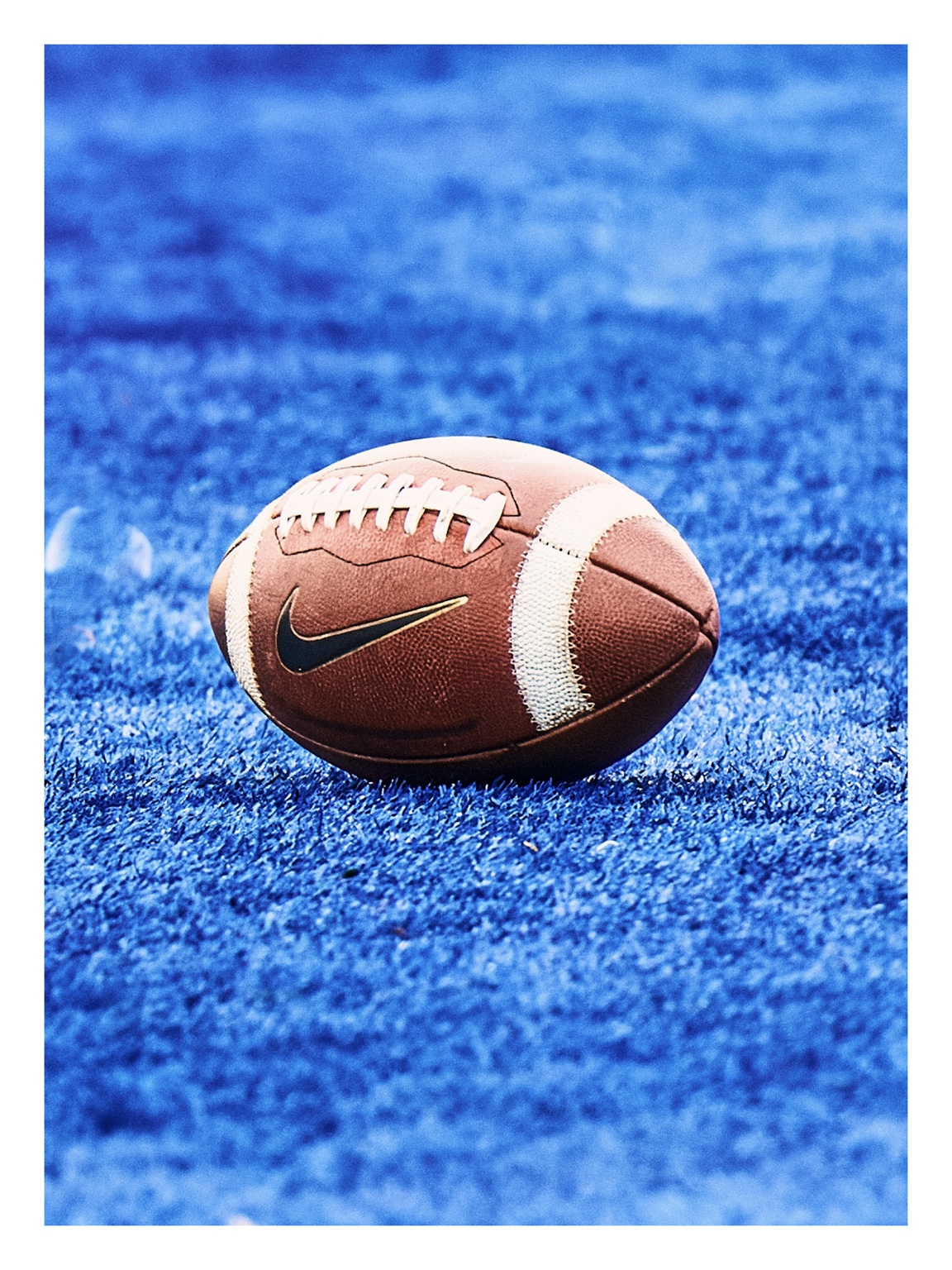 A football resting on vivid blue artificial turf